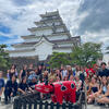 Students posing for photos with a large red cow statue in front of a Japanese castle